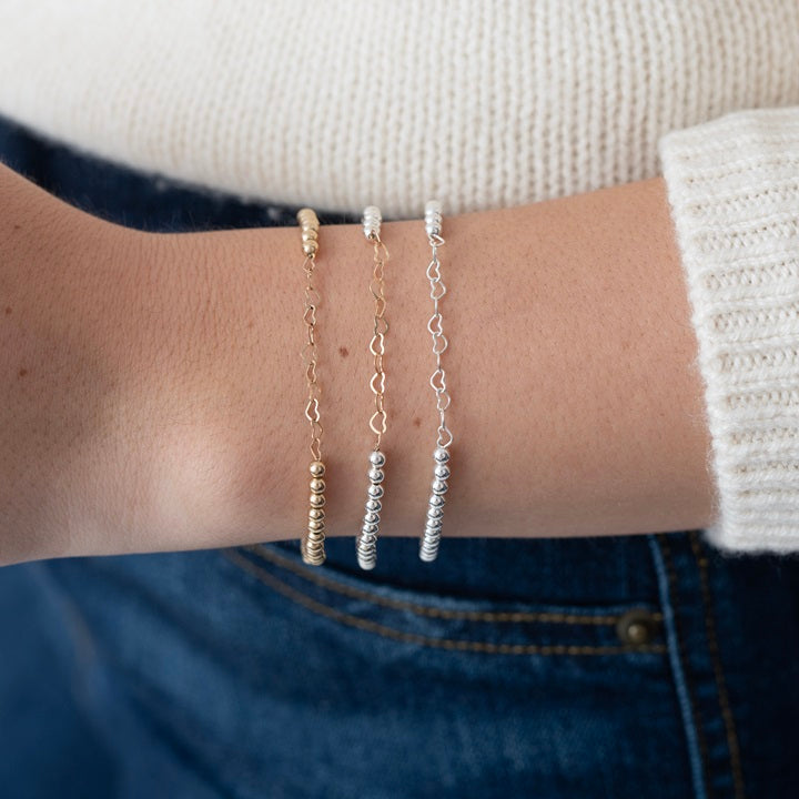 Model wearing gold-filled and sterling silver bracelets with hearts